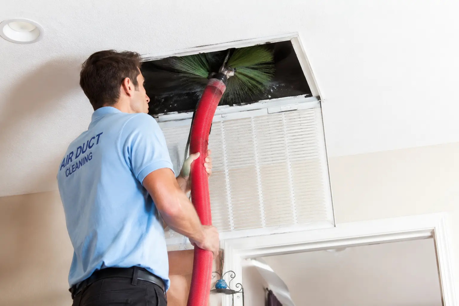 Professional technician cleaning a residential air duct with a specialized brush and vacuum hose.